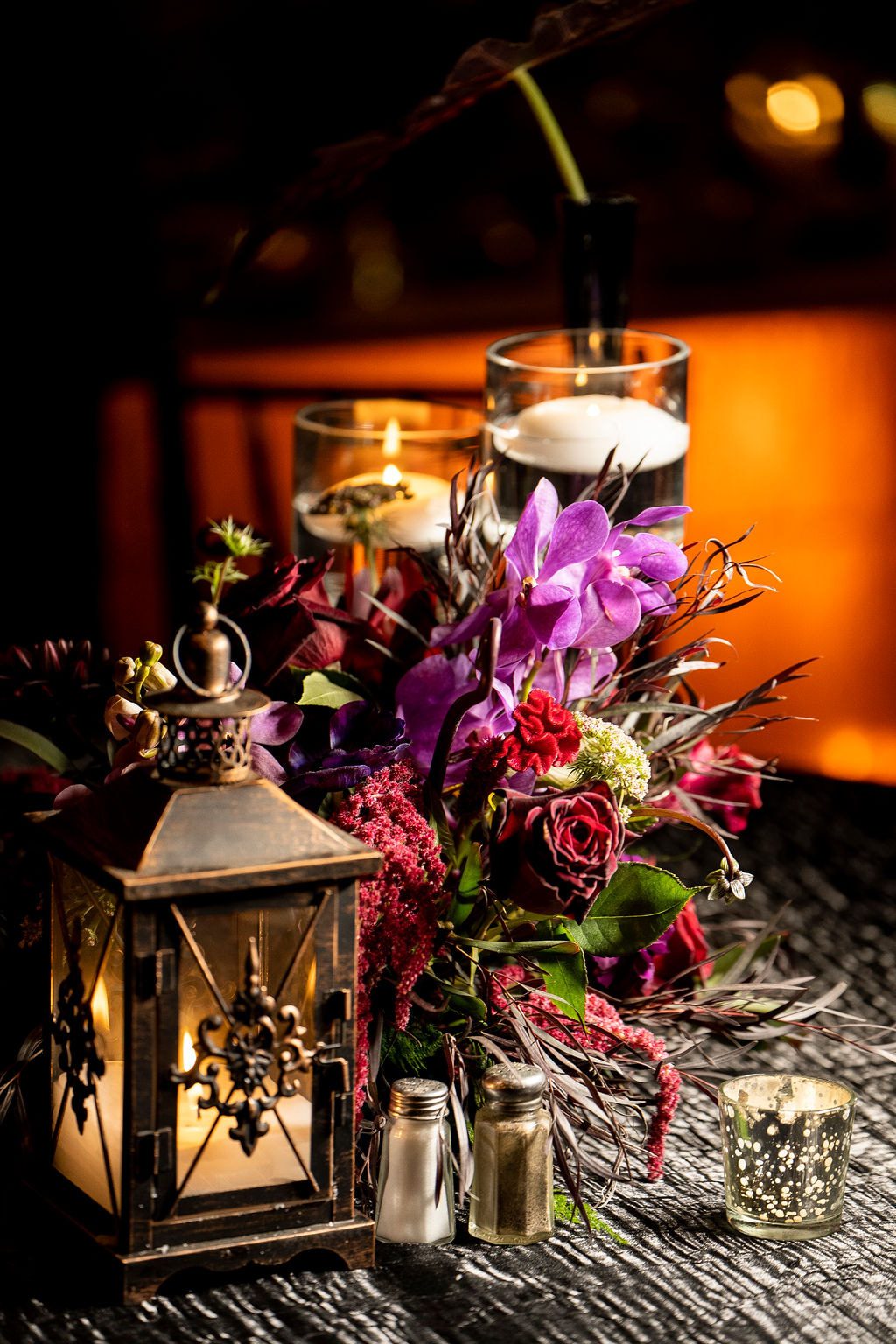 dark moody centerpiece with bronze lantern purple orchid red roses candles
