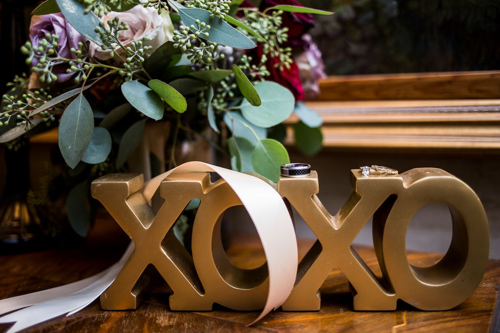 bride and grooms wedding rings with xoxo gold sign and brides bouquet