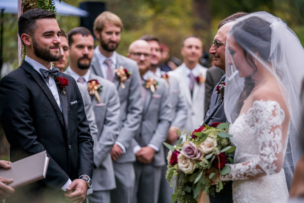 groom smiling at bride while dad gives her away at the altar