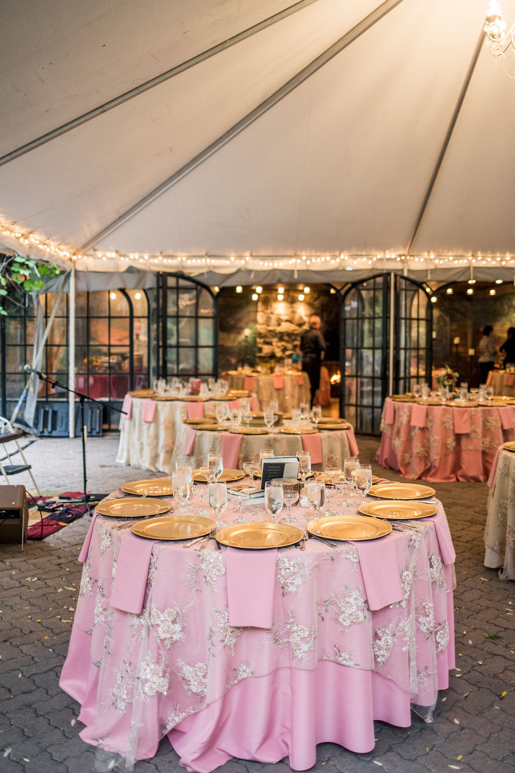 pink tablecloth with beaded overlay with gold chargers at place settings for wedding reception