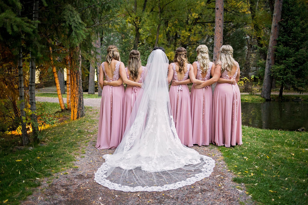 bride and bridesmaids all standing with their backs in pink dresses
