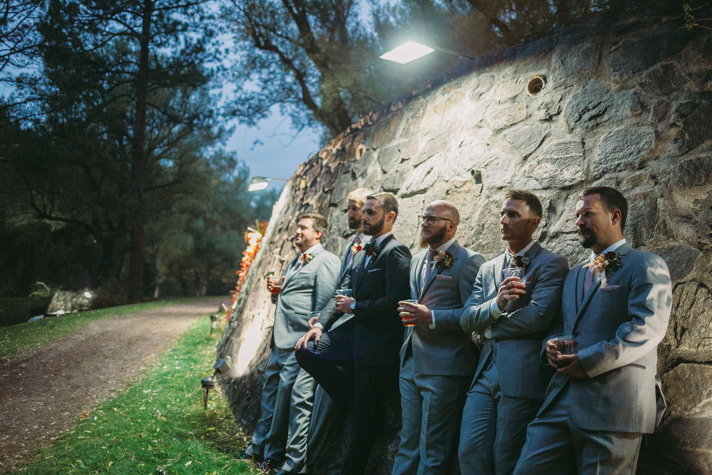 groom and groomsmen lounging on a stone wall with drinks