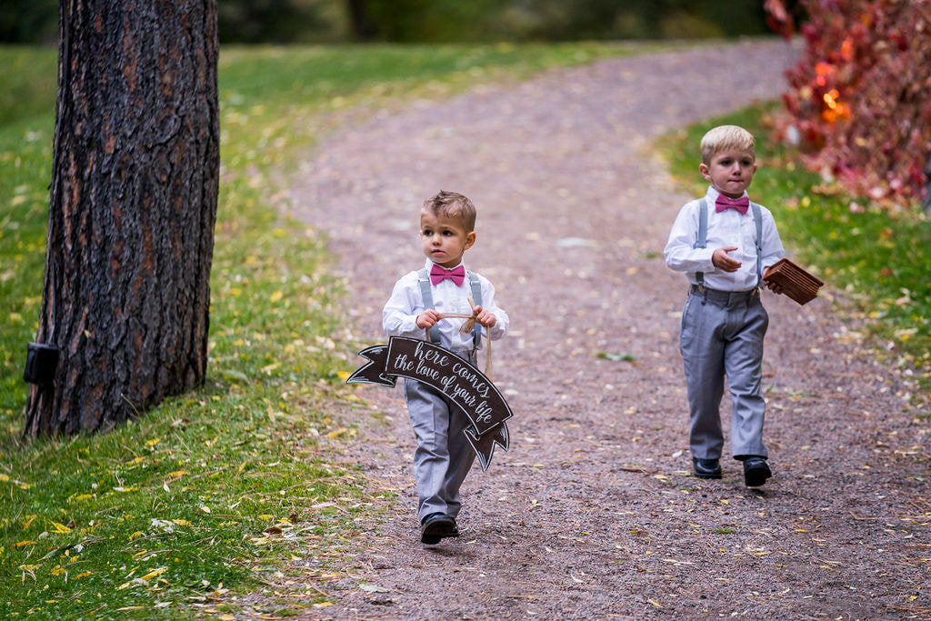two ring bearers in grey suits with pink bowties walking down aisle 