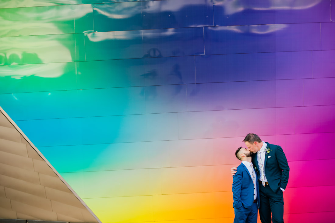 gay couple in front of rainbow wall