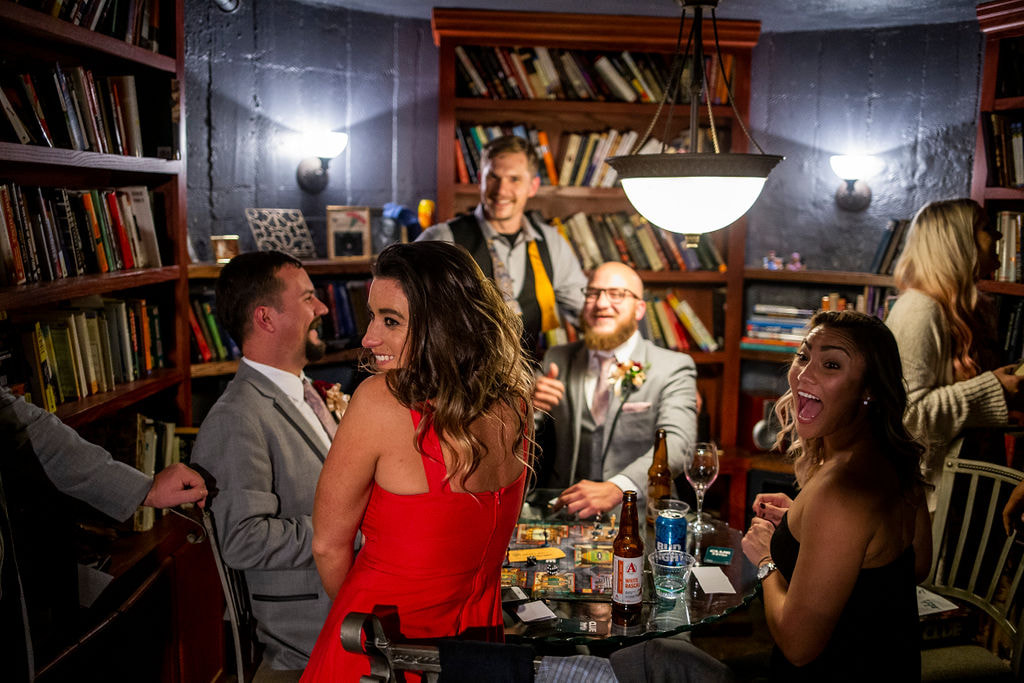 people having fun around a card table with books and drinks in the basement at dunafon castle wedding reception